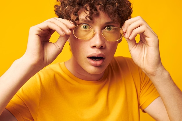 Młody mężczyzna z kręconymi włosami w stylowych okularach w żółtej koszulce pozowanie monochromatyczne zdjęcie