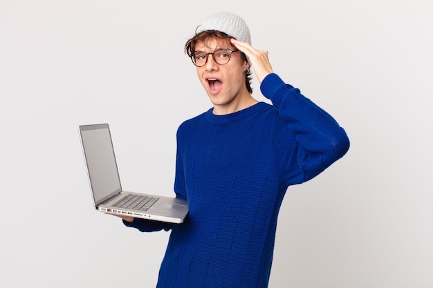 Młody mężczyzna z laptopem wyglądający na szczęśliwego, zdziwionego i zdziwionego