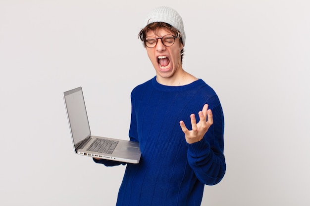Młody mężczyzna z laptopem wyglądający na zły, zirytowany i sfrustrowany