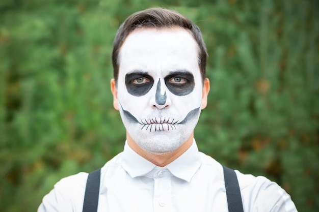 Młody mężczyzna z makijażem szkieletu stoi w lesie na imprezie Halloween