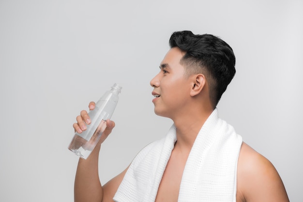 Młody mężczyzna z nagim torsem trzymający butelkę przejrzystego płynu