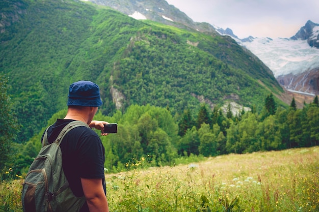 Młody mężczyzna z plecakiem robi zdjęcia górskiego krajobrazu na smartfonie Mężczyzna turysta fotografujący góry na telefonie komórkowym