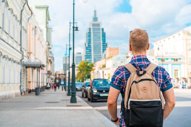 Młody mężczyzna z plecakiem spaceruje letnią moskiewską ulicą z widokiem na wieżowiec