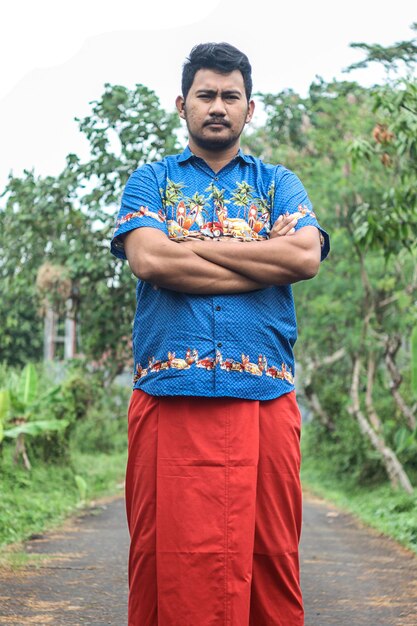 Zdjęcie młody mężczyzna z skrzyżowanymi ramionami w tradycyjnych ubraniach stojący na wiejskiej drodze