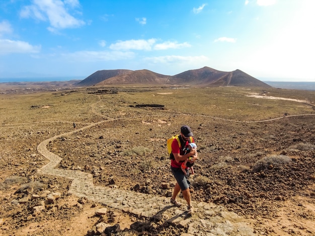 Młody mężczyzna z synem idący ścieżką do krateru wulkanu Calderon Hondo w pobliżu Corralejo, północnego wybrzeża wyspy Fuerteventura, Wyspy Kanaryjskie. Hiszpania