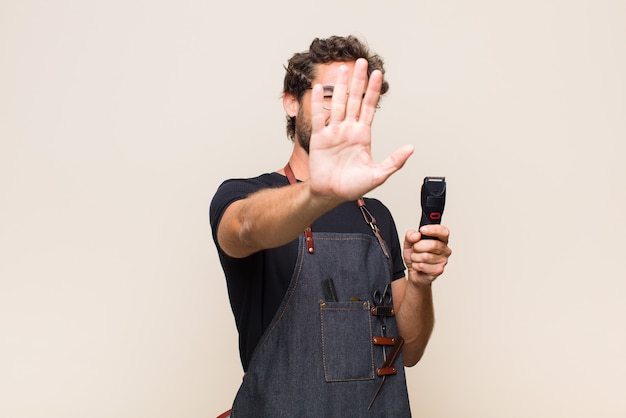 Młody mężczyzna zakrywający twarz ręką i wyciągający drugą rękę do góry, odmawiając zdjęć lub obrazków