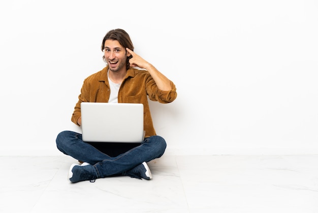 Młody mężczyzna ze swoim laptopem siedzi jeden na podłodze z zamiarem znalezienia rozwiązania