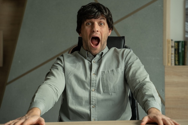 Młody mężczyzna ze zdziwionym wyrazem twarzy siedzi na krześle w biurze