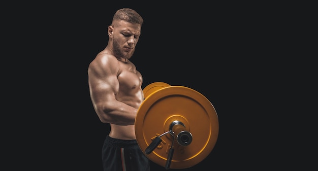 Młody muskularny facet pompuje biceps ze sztangą na czarnym tle. Koncepcja fitness i żywienia. Różne środki przekazu