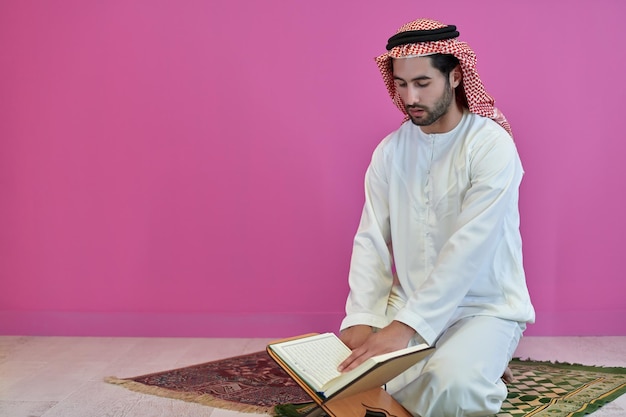 Młody muzułmanin czytający Koran podczas Ramadanu. Arabski chłopiec siedzący samotnie na dywaniku modlitewnym lub macie i recytujący islamską świętą księgę