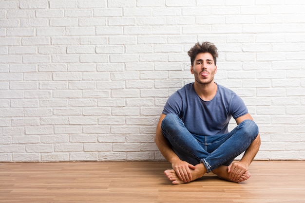 Młody naturalny mężczyzna siedzi na drewnianym podłogowym wyrażeniu zaufanie i emocja