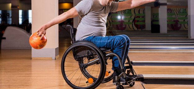 Młody niepełnosprawny mężczyzna na wózku inwalidzkim grający w kręgle w klubie