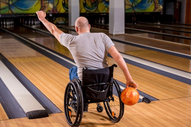 Młody niepełnosprawny mężczyzna na wózku inwalidzkim grający w kręgle w klubie