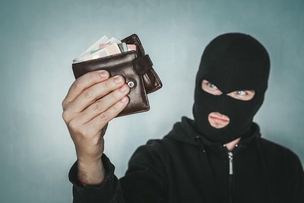 Zdjęcie młody nieumyślny mężczyzna w czarnej masce trzyma czarną skórzaną torebkę i patrzy na swój łup złodziej ukradł portfel pół strzału złodzieja w kominiarce z torebką sprawa kieszonkowca
