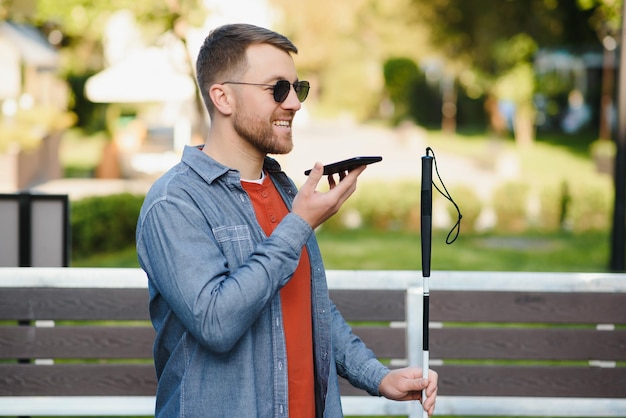 Młody niewidomy mężczyzna używający telefonu i wysyłający wiadomość głosową