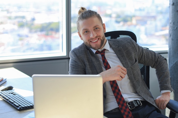Młody nowoczesny biznes człowiek pracuje za pomocą laptopa siedząc w biurze.