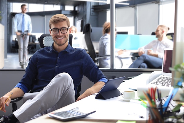 Młody nowoczesny biznesowy mężczyzna pracujący przy użyciu cyfrowego tabletu siedząc w biurze