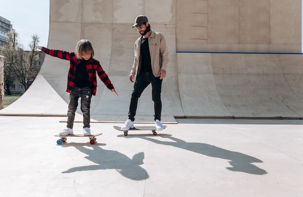 Młody Ojciec I Jego Syn Jeżdżą Na Deskorolkach W Skateparku Ze Zjeżdżalniami Na Zewnątrz W Słoneczny Dzień.