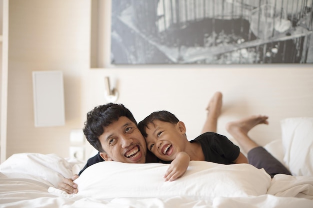 Młody ojciec i mały chłopiec bawią się wesoło na łóżku w pokoju hotelowym na wakacjach
