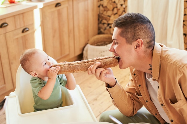 Zdjęcie młody ojciec i syn jedzą bagietkę w kuchni