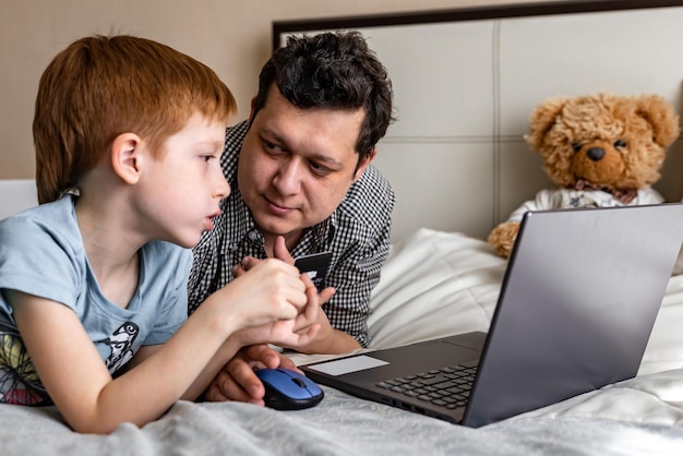 Młody ojciec i syn zakupy razem online płatność internetowa czas dla rodziny Dziecko rudowłosy chłopiec i tata przy laptopie wybierają zakupy pomyślał mężczyzna