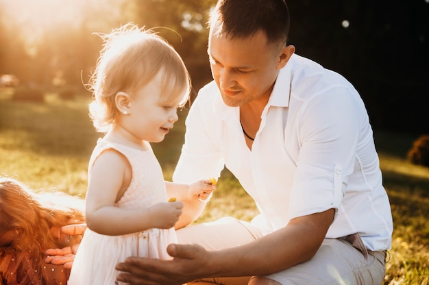 Młody ojciec obejmujący swoją małą córeczkę. Mała dziewczynka bawi się z ojcem przed zachodem słońca na świeżym powietrzu.