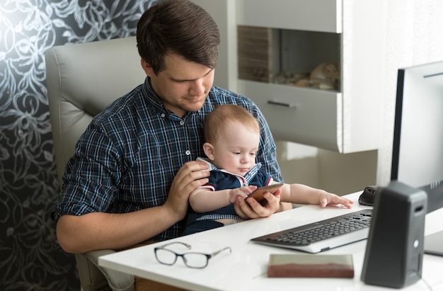 Młody ojciec pracuje przy komputerze bawi się ze swoim synkiem