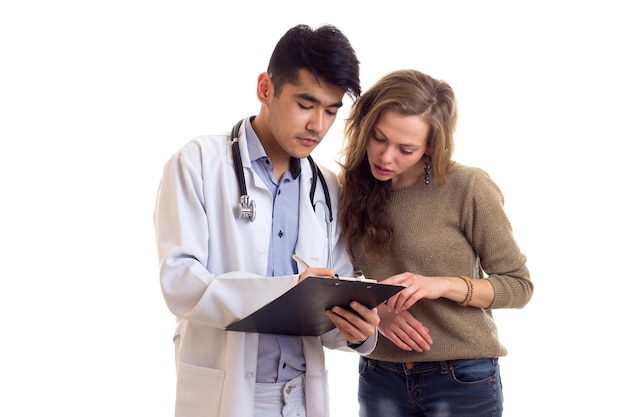 Młody pewny siebie lekarz w białej sukni ze stetoskopem patrzący na papiery z młodą miłą kobietą