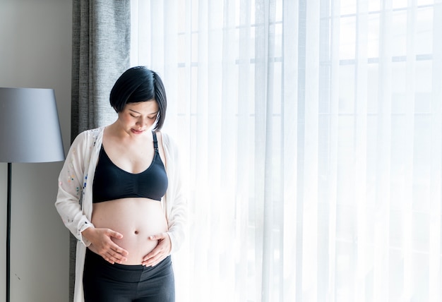 Młody piękny Azjatycki kobieta w ciąży dotyka jej brzucha w domu