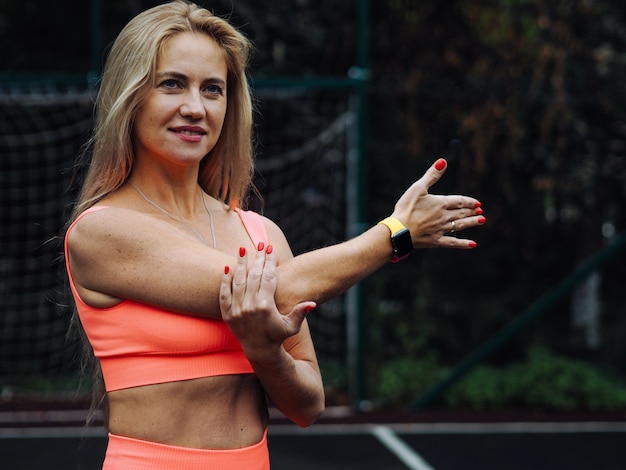 Młody piękny blond fitness model z długimi włosami w neonowej pomarańczowej odzieży sportowej robi ćwiczenia rozciągające