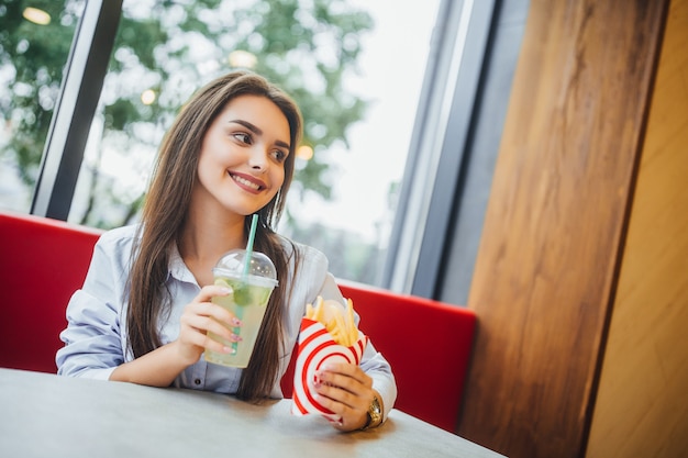 Młody piękny kobiety mienia hamburger i mohito w fast food restauraci