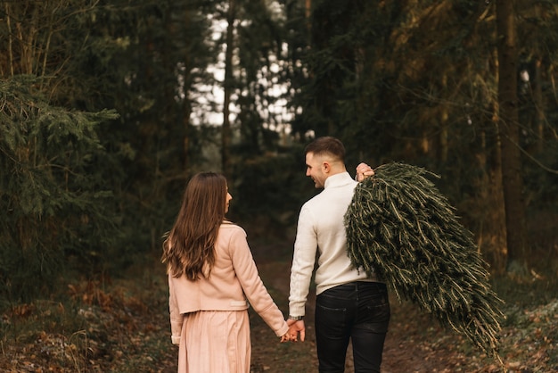 Młody piękny szczęśliwy kochankowie mężczyzna i kobieta, historia miłosna zimą z żywą choinką w sosnowym lesie w słońcu