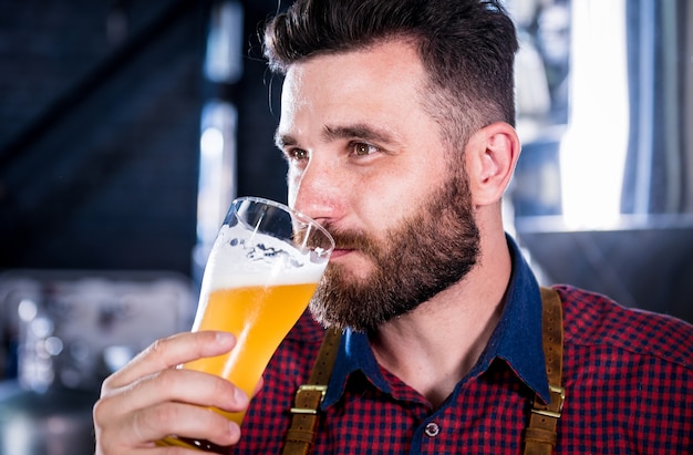Młody piwowar w skórzanym fartuchu testuje piwo w nowoczesnym browarze