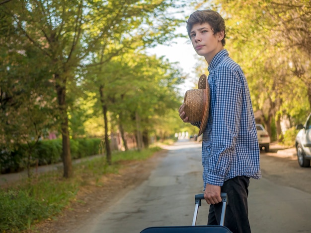 Młody podróżny nastolatek ciągnie dużą walizkę w lato miasta ulicie