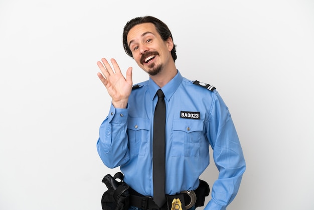 Młody policjant na białym tle pozdrawiając ręką ze szczęśliwym wyrazem twarzy