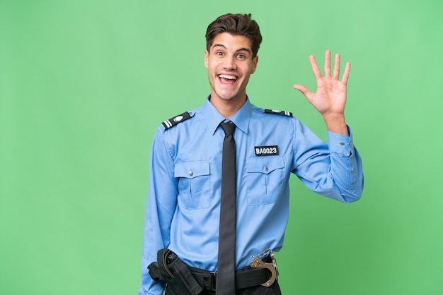 Młody policjant na odosobnionym tle pozdrawiający ręką z radosnym wyrazem twarzy
