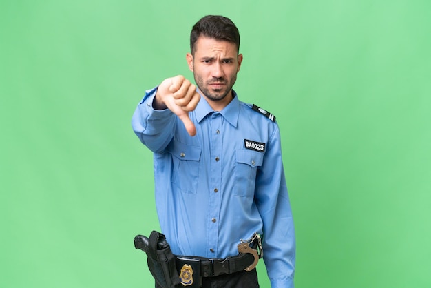 Młody policyjny kaukaski mężczyzna na odosobnionym tle pokazuje kciuk w dół z negatywnym wyrazem twarzy
