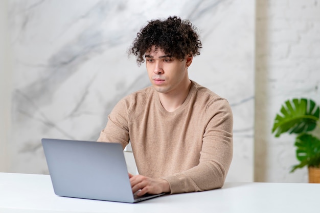Młody poważny łaciński etniczny mężczyzna przystojny facet freelancer pracuje na swoim laptopie, patrząc na