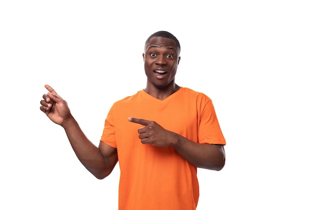 Młody, pozytywny, szczęśliwy Amerykanin w pomarańczowej koszulce wskazuje palcem na obecność interesujących