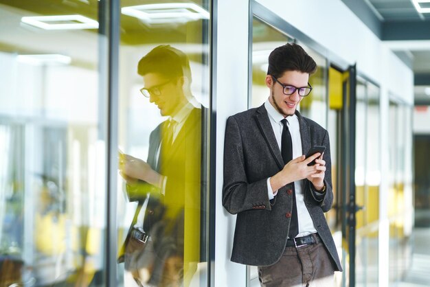 Młody pracownik biurowy w okularach przy użyciu inteligentnego telefonu komórkowego Biznesmen trzyma telefon w ręku