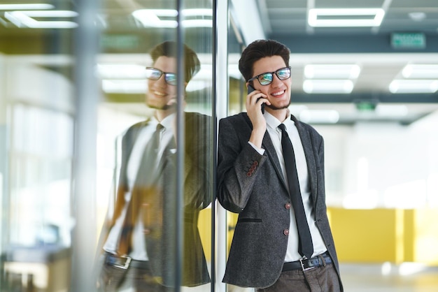 Młody pracownik biurowy w okularach przy użyciu inteligentnego telefonu komórkowego Biznesmen trzyma telefon w ręku