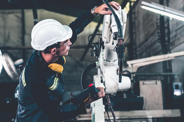 Młody pracownik fabryki pracujący z doświadczonym ramieniem robota