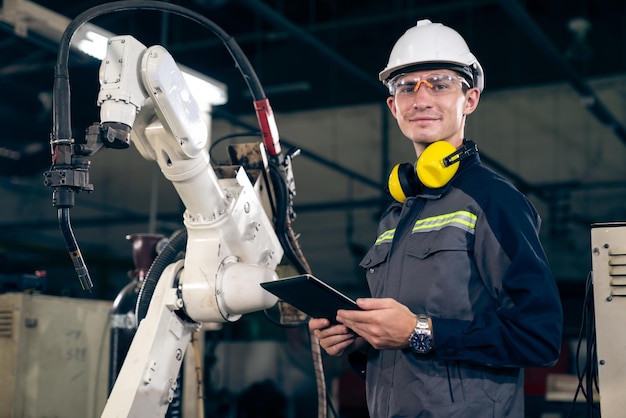 Młody pracownik fabryki pracujący z doświadczonym ramieniem robota