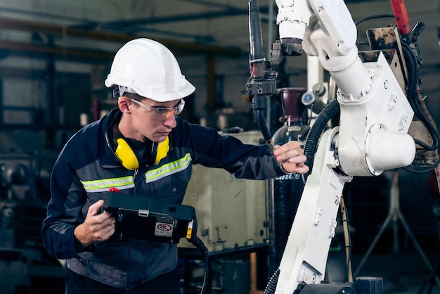 Młody pracownik fabryki pracujący z doświadczonym ramieniem robota