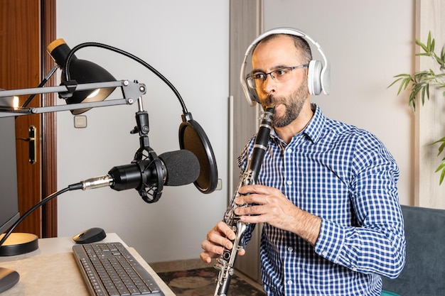 Młody przedsiębiorca gra na klarnecie w domu i nagrywa muzykę, aby przesyłać ją strumieniowo online za pomocą swojego komputera