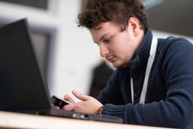 Młody przypadkowy biznesmen używający smartfona w biurze startupu