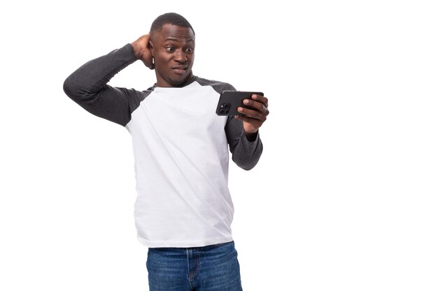 Młody przystojny Amerykanin ubrany w sweter z długimi rękawami czyta informacje przez telefon