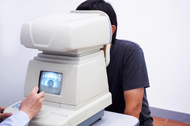 Młody, przystojny Azjat poddał się badaniu wzroku za pomocą optycznej maszyny do badań wzroku.