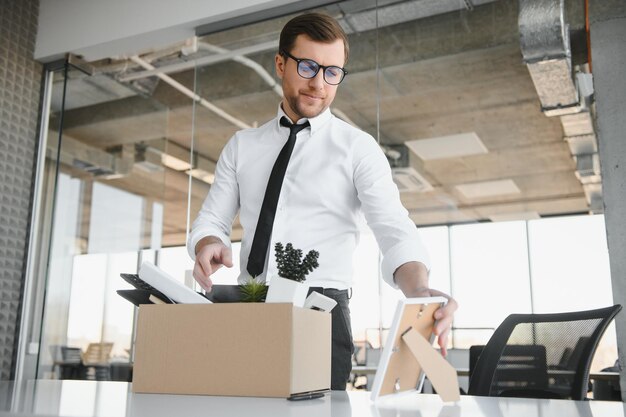 Zdjęcie młody przystojny biznesmen w lekkim nowoczesnym biurze z pudełkiem kartonowym ostatni dzień w pracy zdenerwowany pracownik biurowy zostaje zwolniony