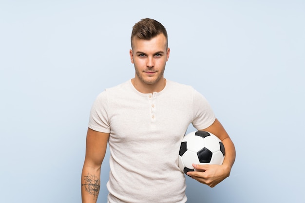 Młody Przystojny Blondynka Mężczyzna Nad Odosobnioną Błękit ścianą Trzyma Piłki Nożnej Piłkę